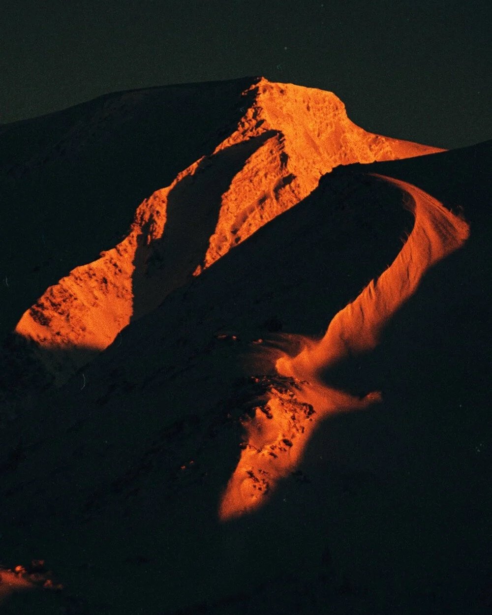 montagne enneigée illuminée par la lumière orange du coucher du soleil ou du lever du soleil, dans l'obscurité de la nuit