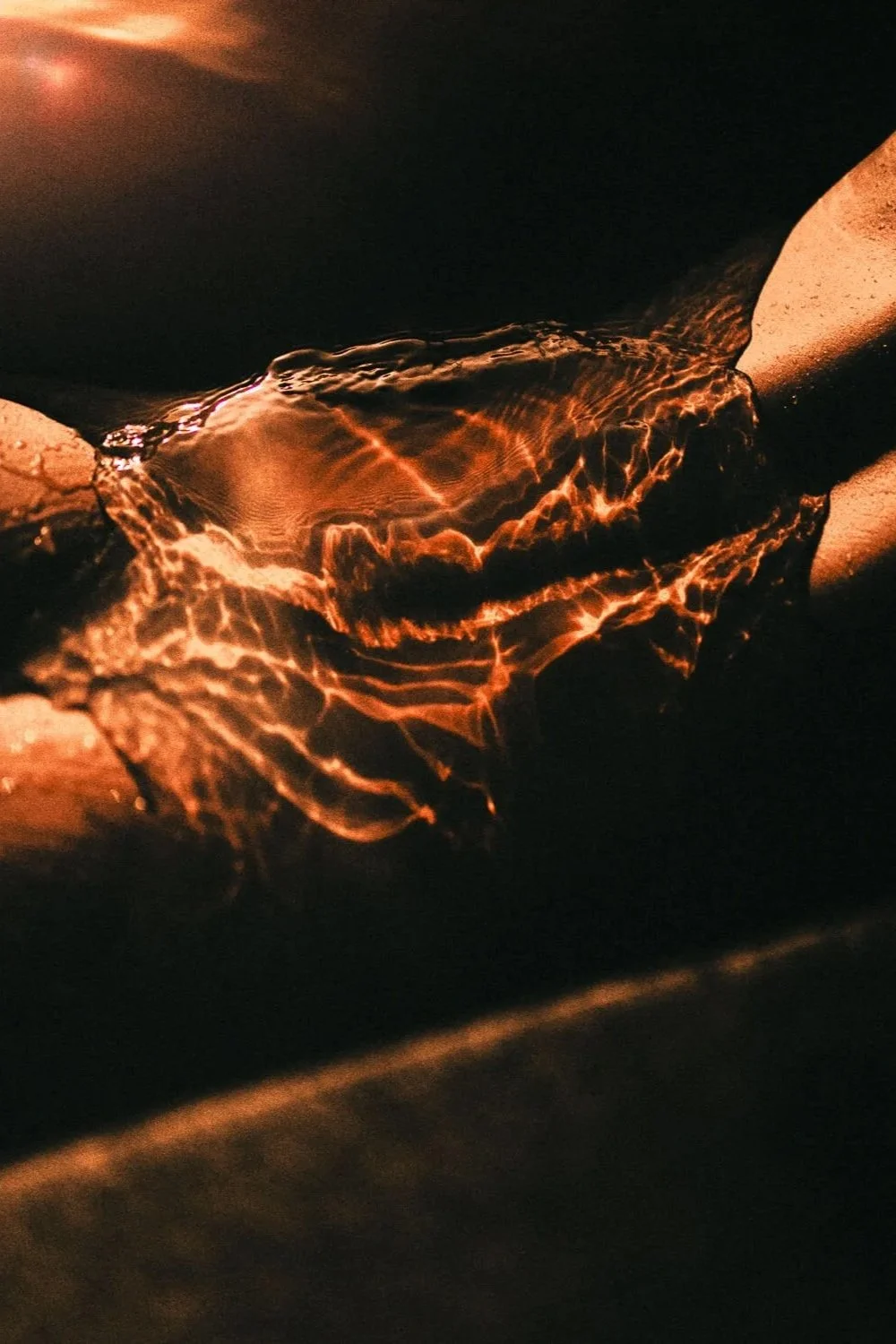 Une photographie artistique de l'eau en train de couler entre deux pierres, avec des reflets orange chaud sur la surface de l'eau dans l'obscurité.