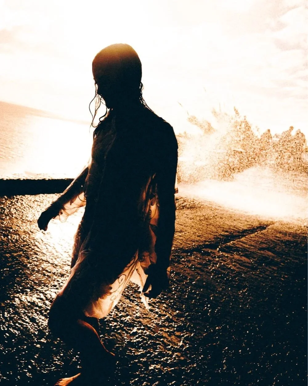 Silhouette d'une femme dans l'eau au coucher du soleil avec des vagues en arrière-plan