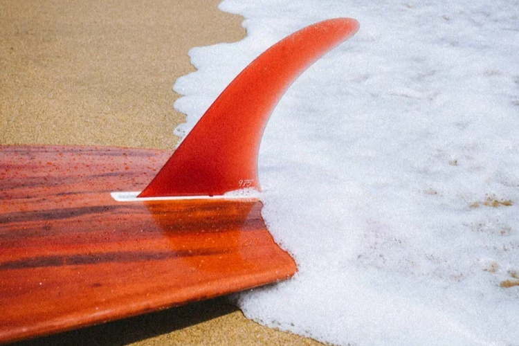 Une planche de surf rouge avec une nageoire à l'arrière, posée sur la plage avec des vagues qui l'entourent.
