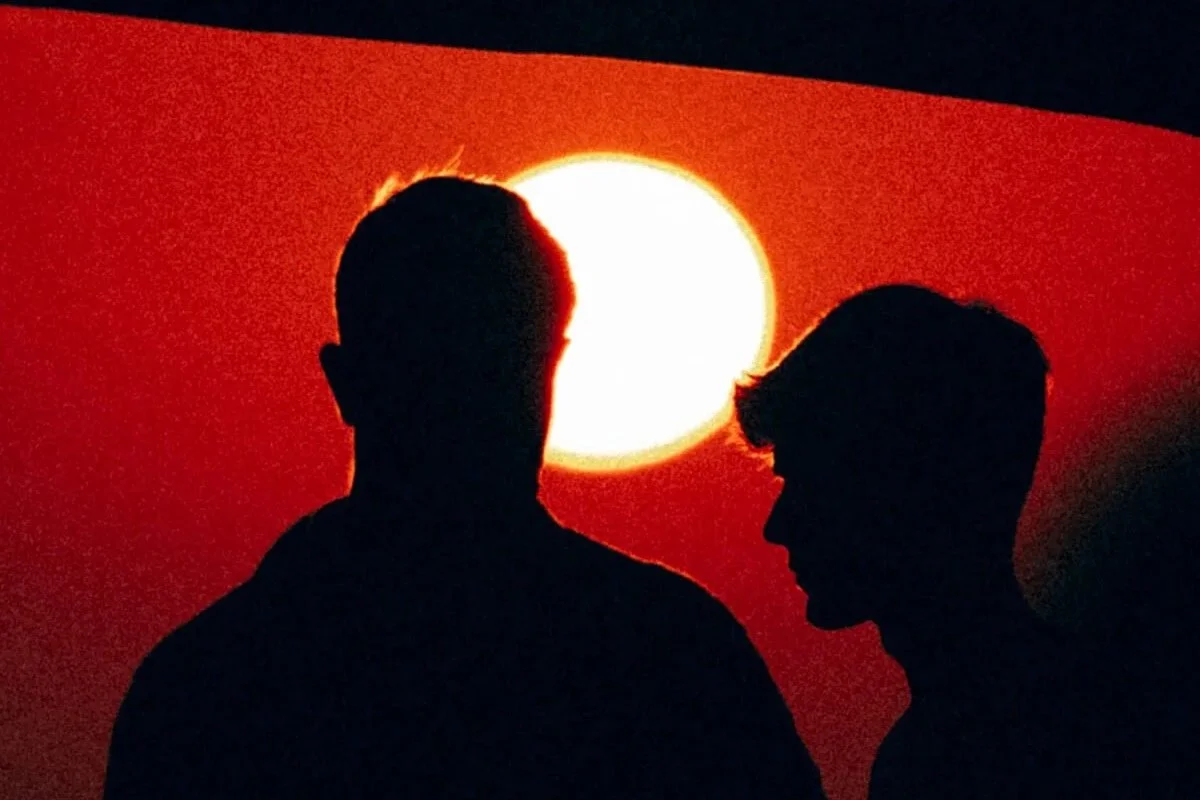 Silhouettes de deux personnes devant un coucher de soleil rouge vif.
