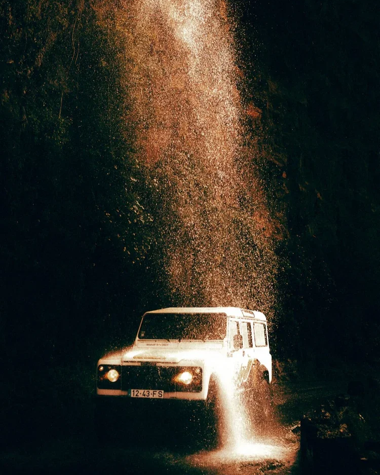 Un véhicule tout-terrain blanc en mouvement en pleine nuit, avec de la poussière ou de l'eau qui s'envole en raison de sa vitesse, créant un phénomène de diffusion colloïdal.