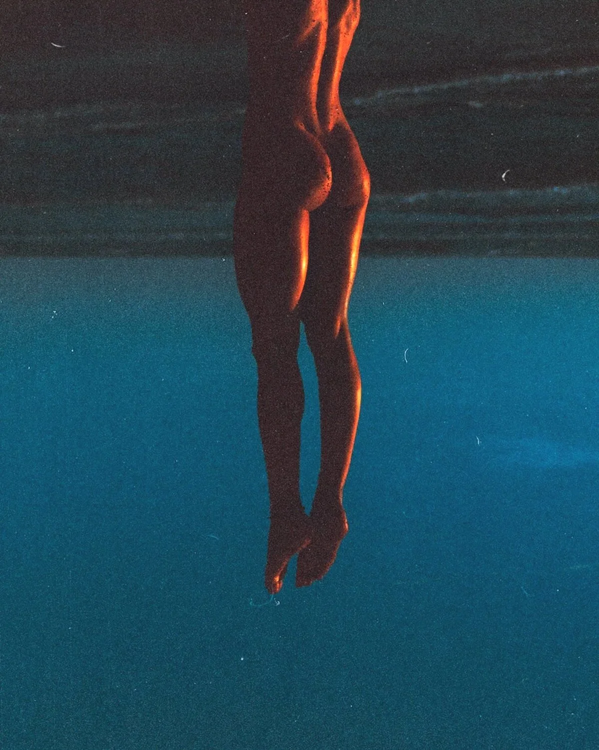 Silhouette d'une personne flottant verticalement dans l'eau, éclairée par une lumière orangée, avec un effet de réflexion.