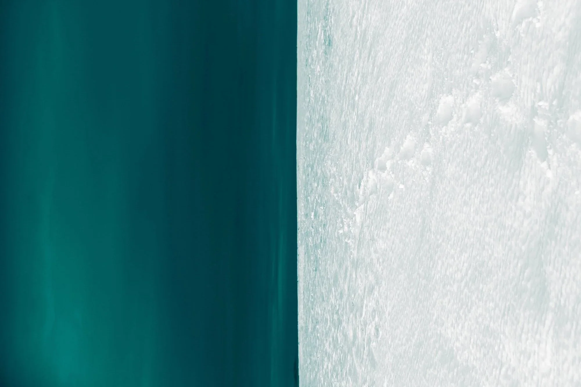 Close-up of a snowy or icy surface with textured ice on the right and blurred blue-green background on the left.
