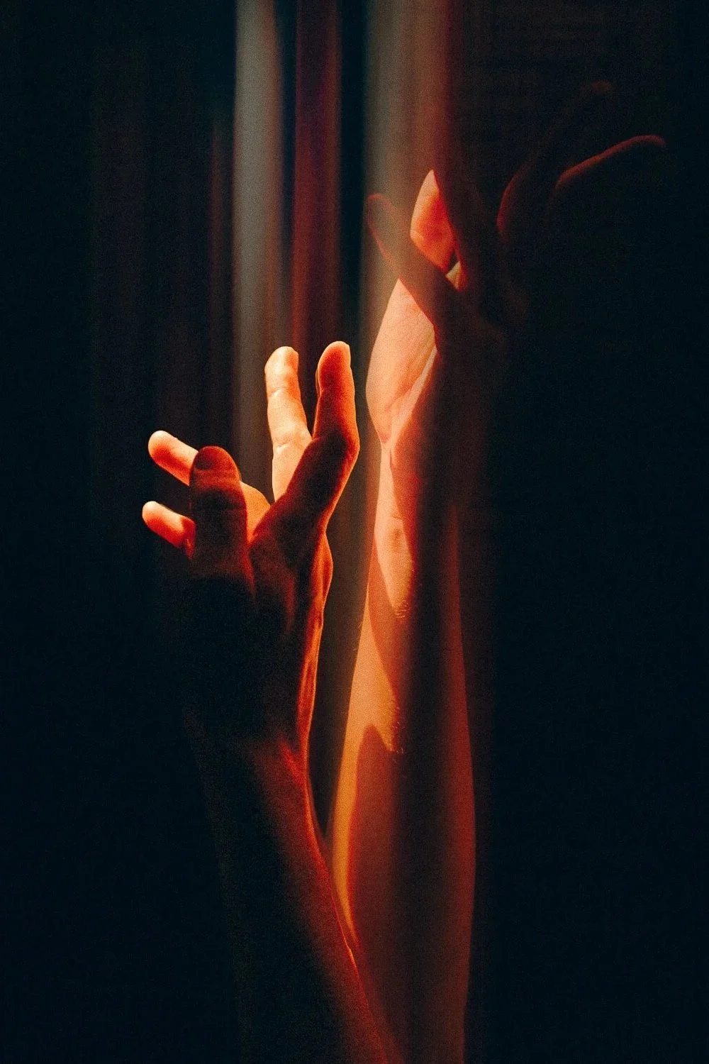 Une main humaine touchant une vitre ou une surface transparente, avec une lumière chaleureuse et un fond sombre.