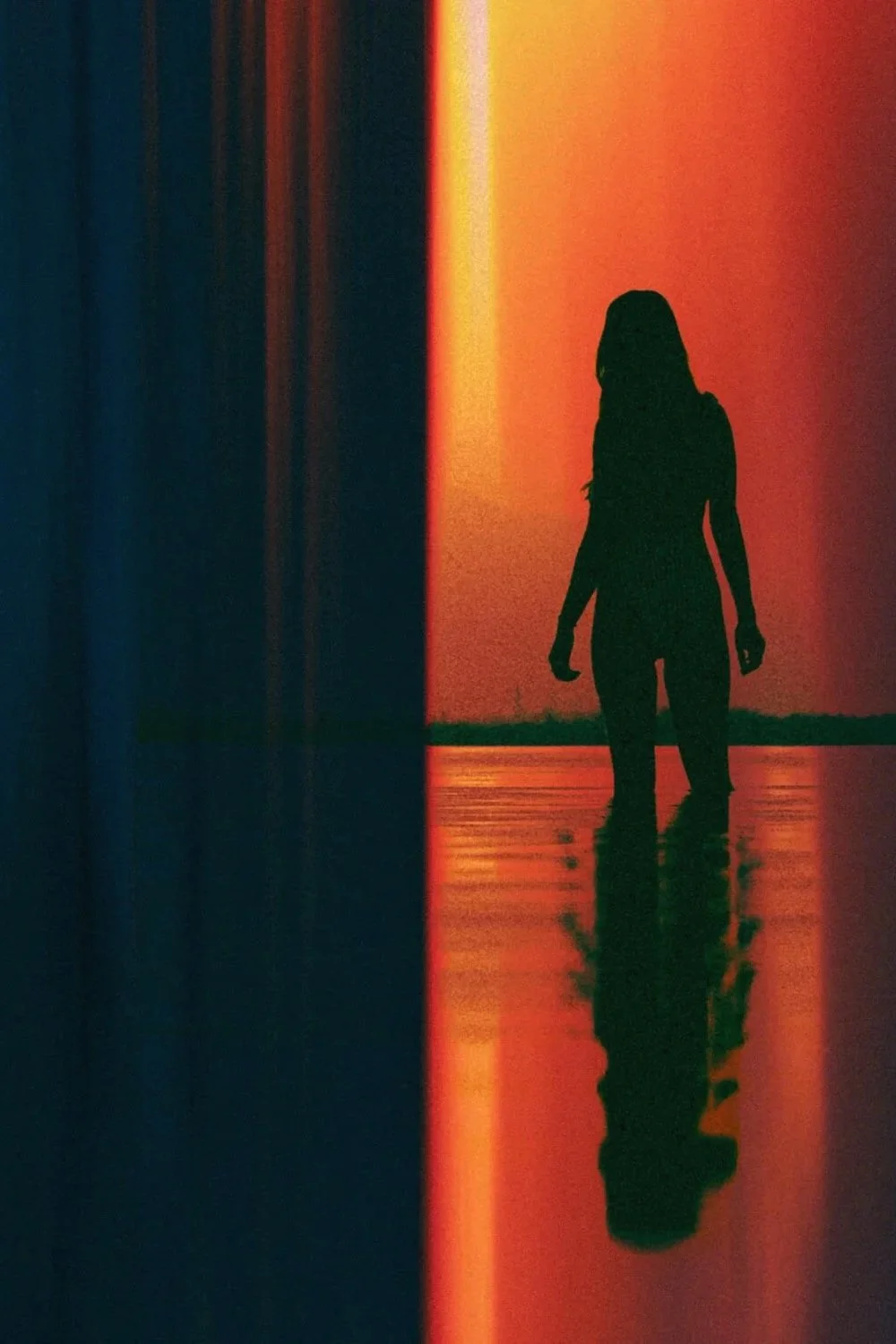 Silhouette d'une personne marchant dans l'eau avec un coucher de soleil vibrant en arrière-plan.