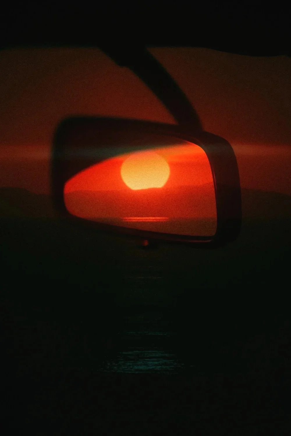 Coucher de soleil vu à travers un rétroviseur latéral de voiture, avec des tons rouges et oranges lumineux.