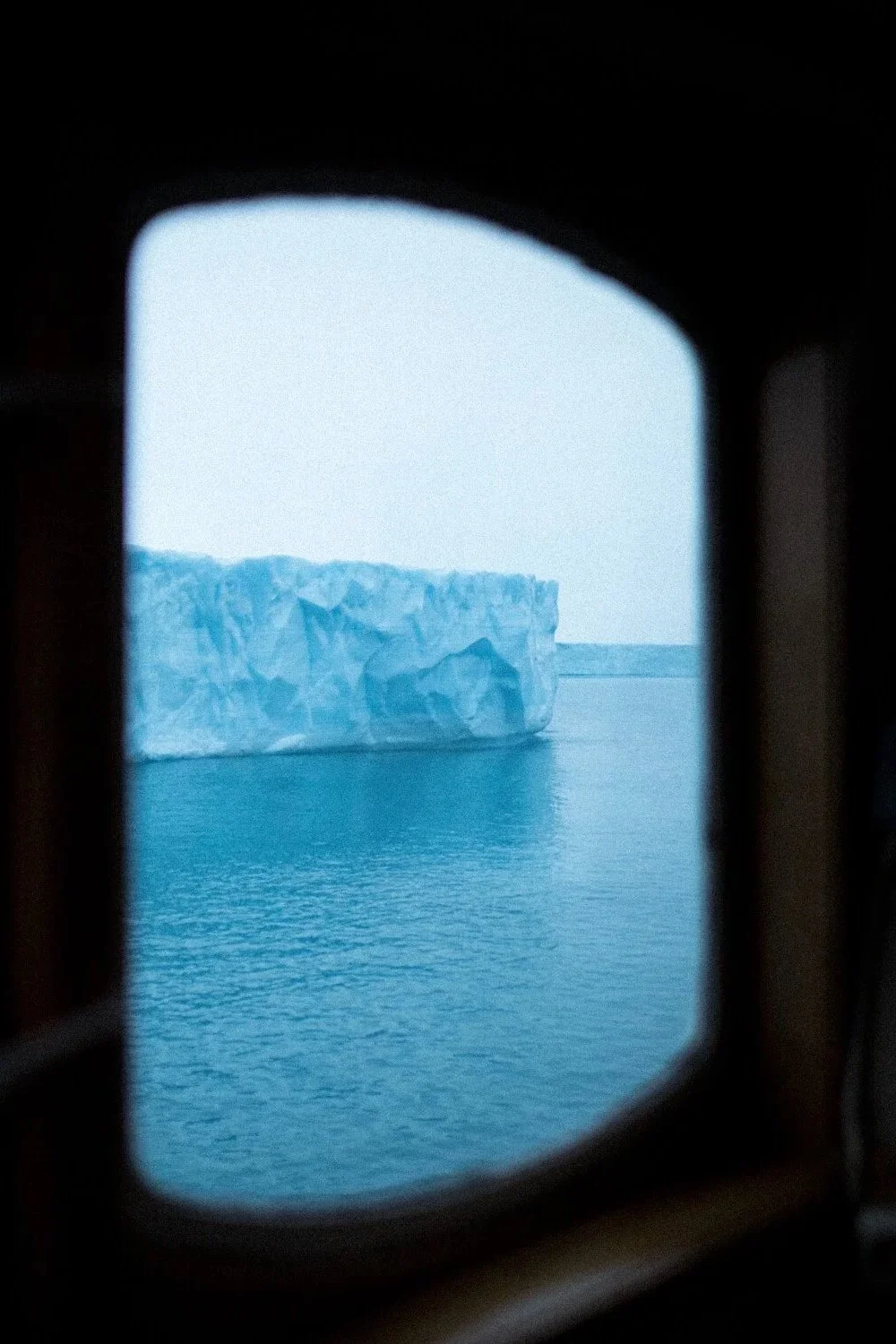Vue d'un iceberg flottant dans l'eau, observé à travers un hublot.
