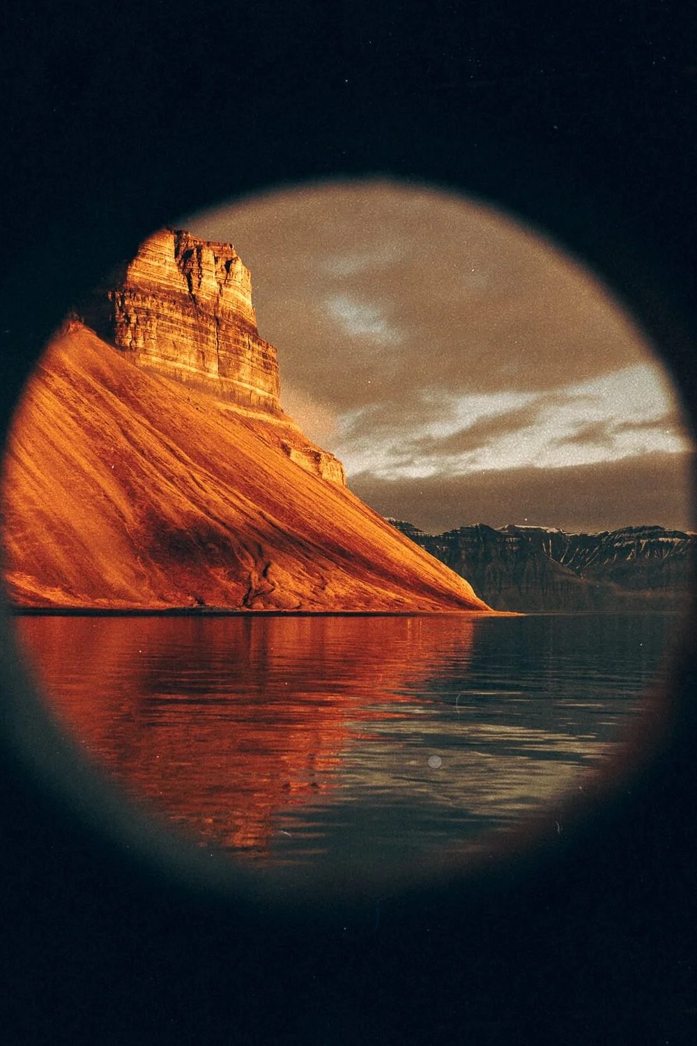 Vue circulaire d'une montagne orange reflétée dans l'eau, avec un ciel nuageux.