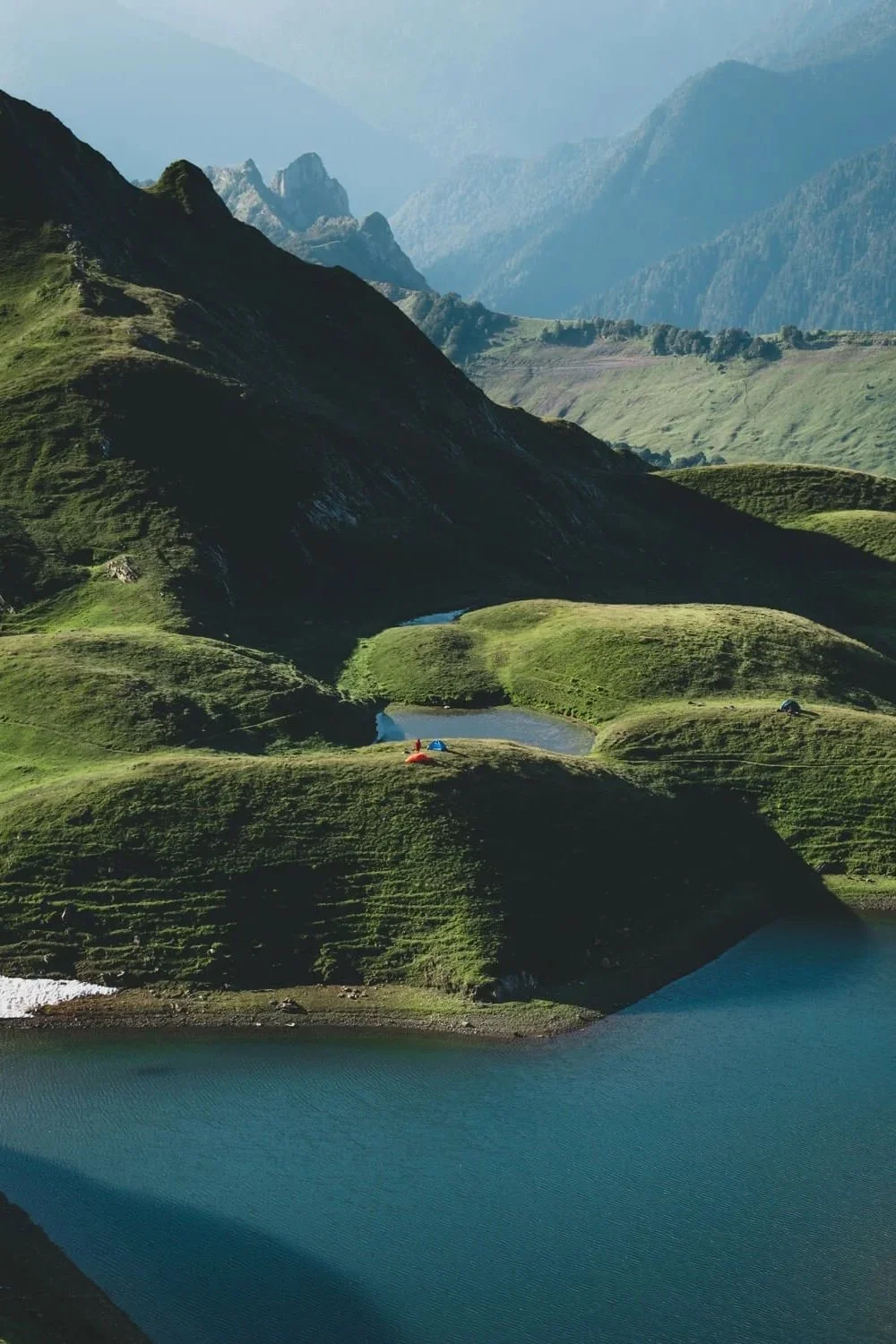 Paysage de montagne avec collines verdoyantes, tentes colorées et lacs alpins.