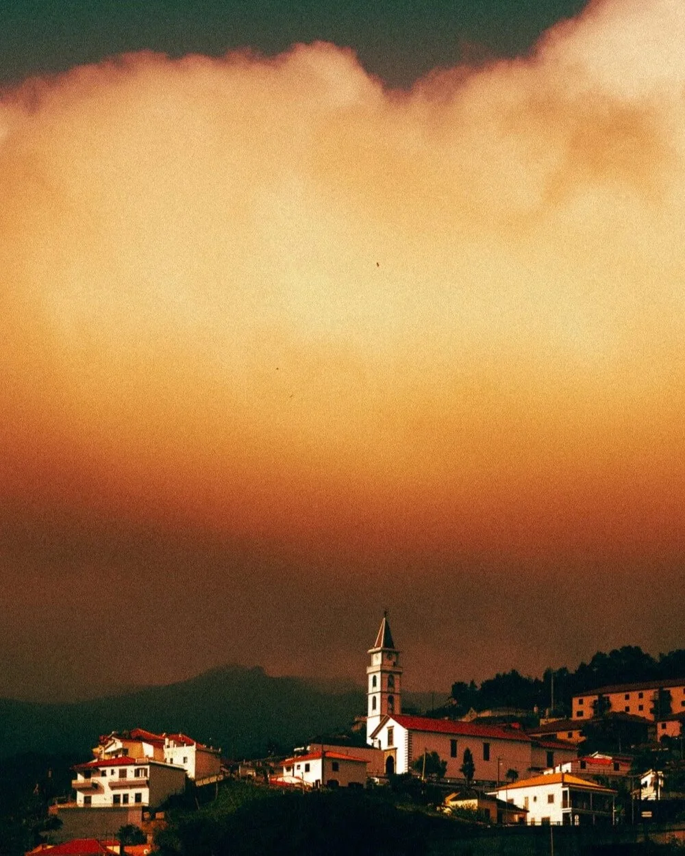 Vue d'un village avec des maisons et une église avec un clocher, sous un ciel orageux ou en pleine tombée de nuit.