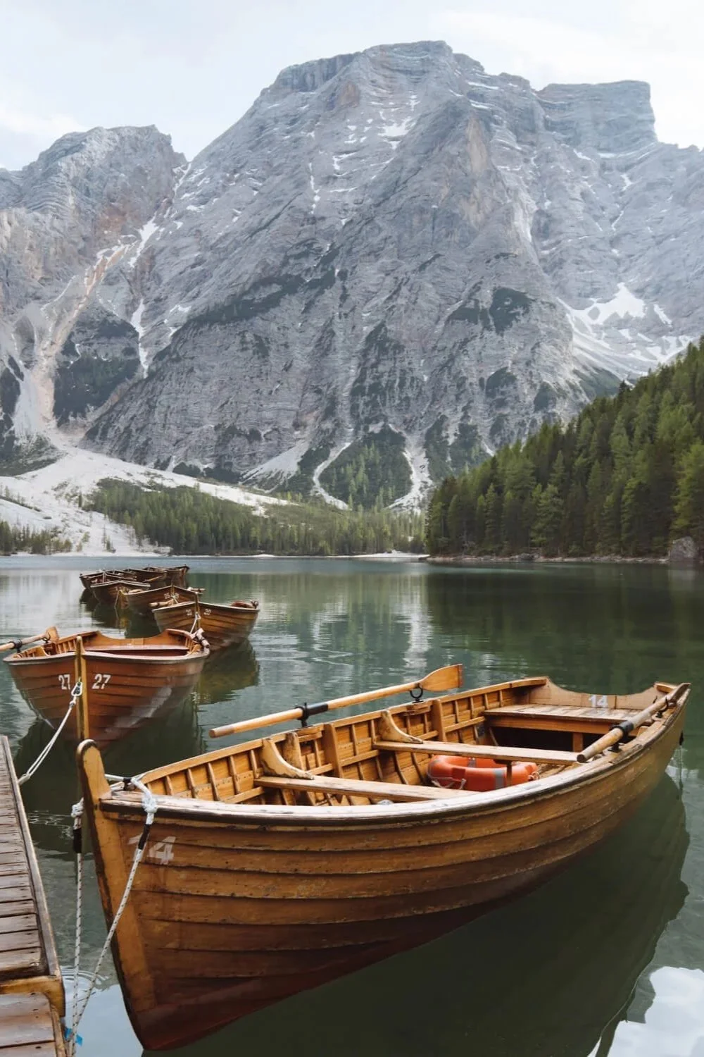 Bateaux en bois sur un lac calme avec des montagnes majestueuses en arrière-plan et des forêts de pins.