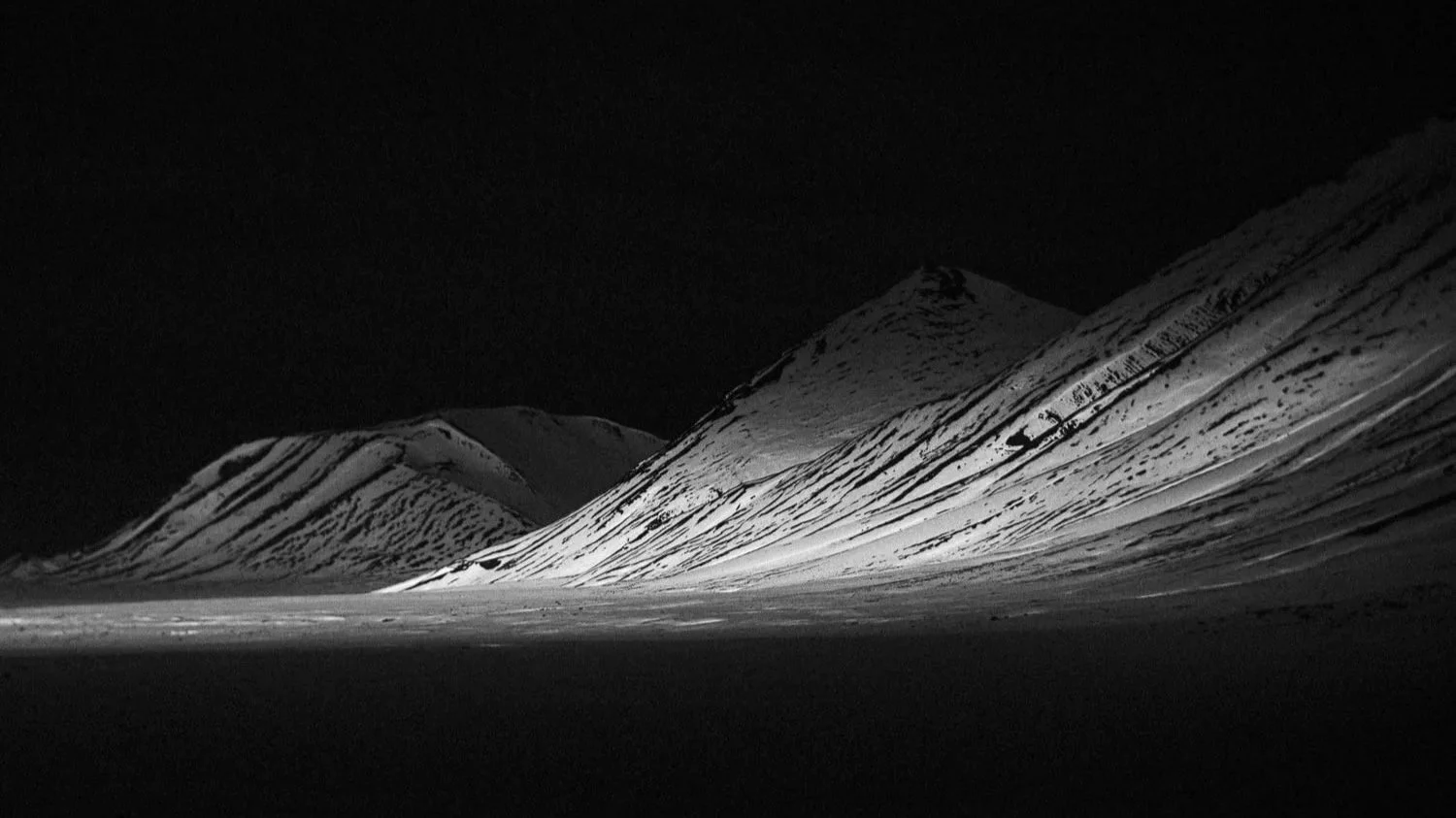 Paysage de montagnes enneigées éclairées la nuit, avec un fond sombre.