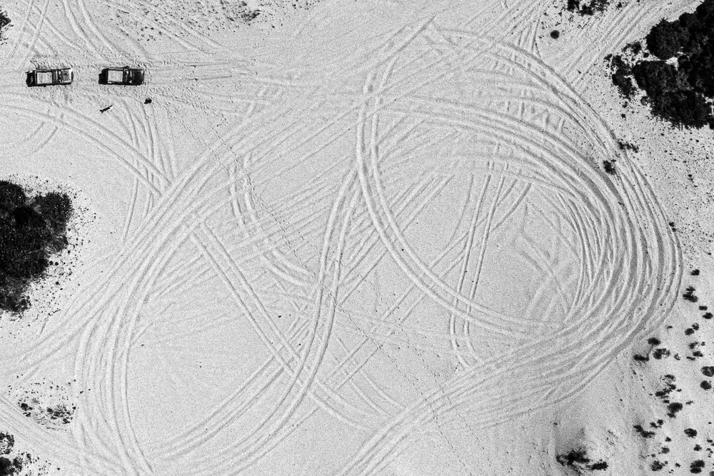 Two vehicles driving on a snow-covered area leaving tire marks in circular and linear patterns