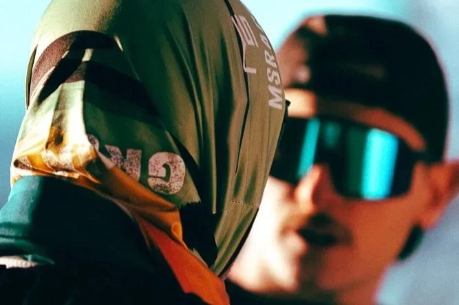 Two people, one in a camouflage jacket and the other in sunglasses and a cap, outdoors.