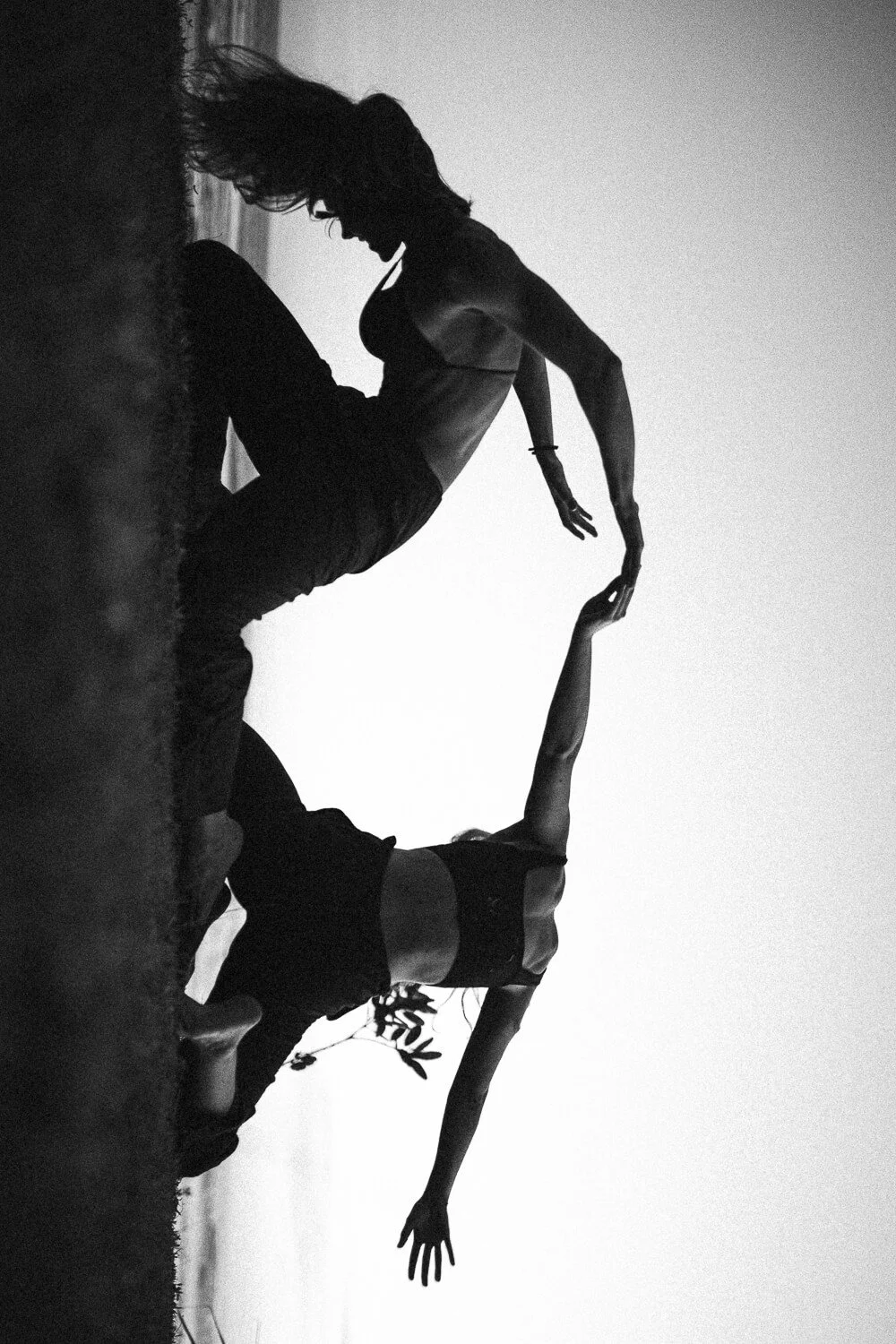 Black and white photo of two women practicing acro yoga outdoors at sunset, balancing on their hands with one leg extended upward.