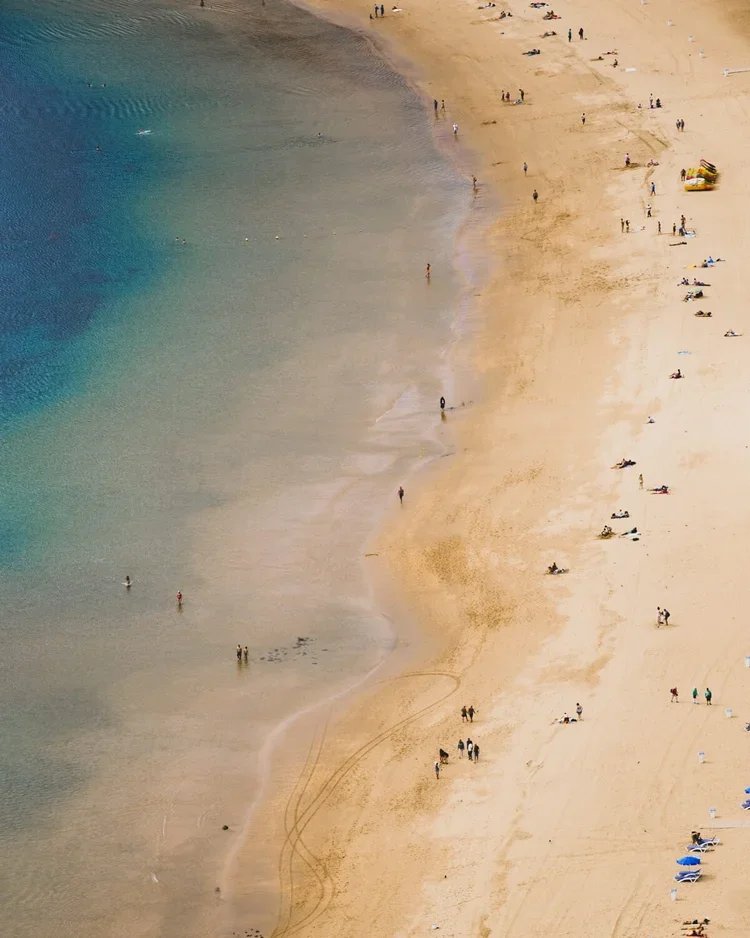 Plage de sable avec des personnes se baignant et se relaxant, vue aérienne.