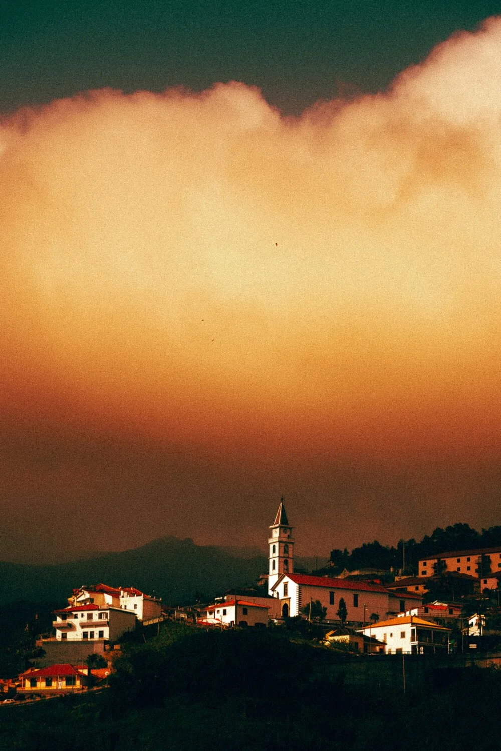 Vue d'un village avec des maisons et une église avec un clocher, sous un ciel orageux ou en pleine tombée de nuit.