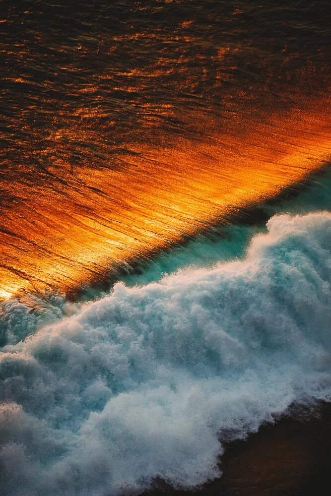 Ocean waves crashing with the reflection of a sunset on the water surface.