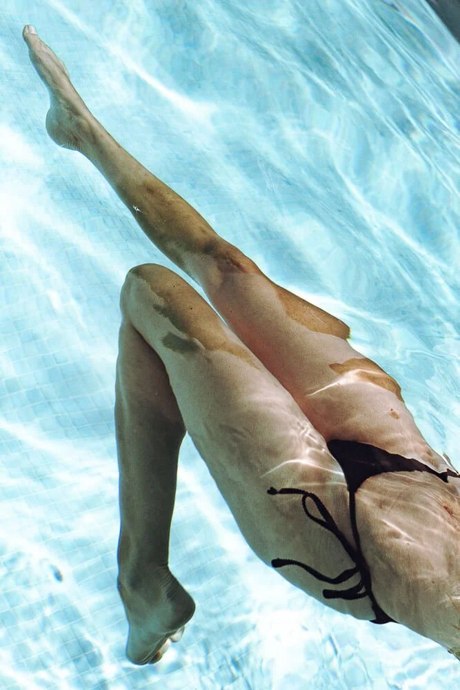 Person swimming underwater in a pool, wearing a black bikini.
