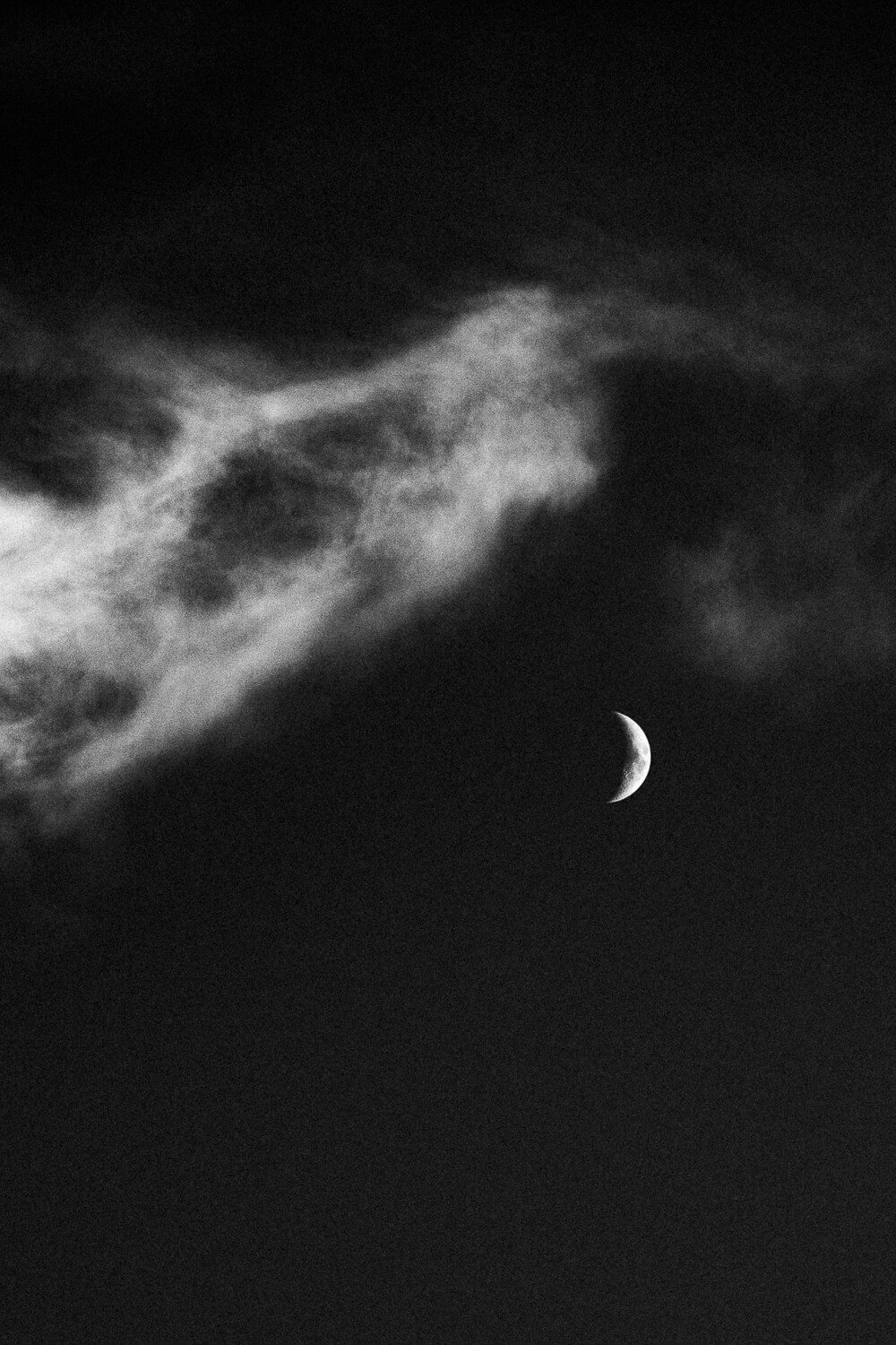 Black and white photo of a crescent moon with clouds in the night sky.