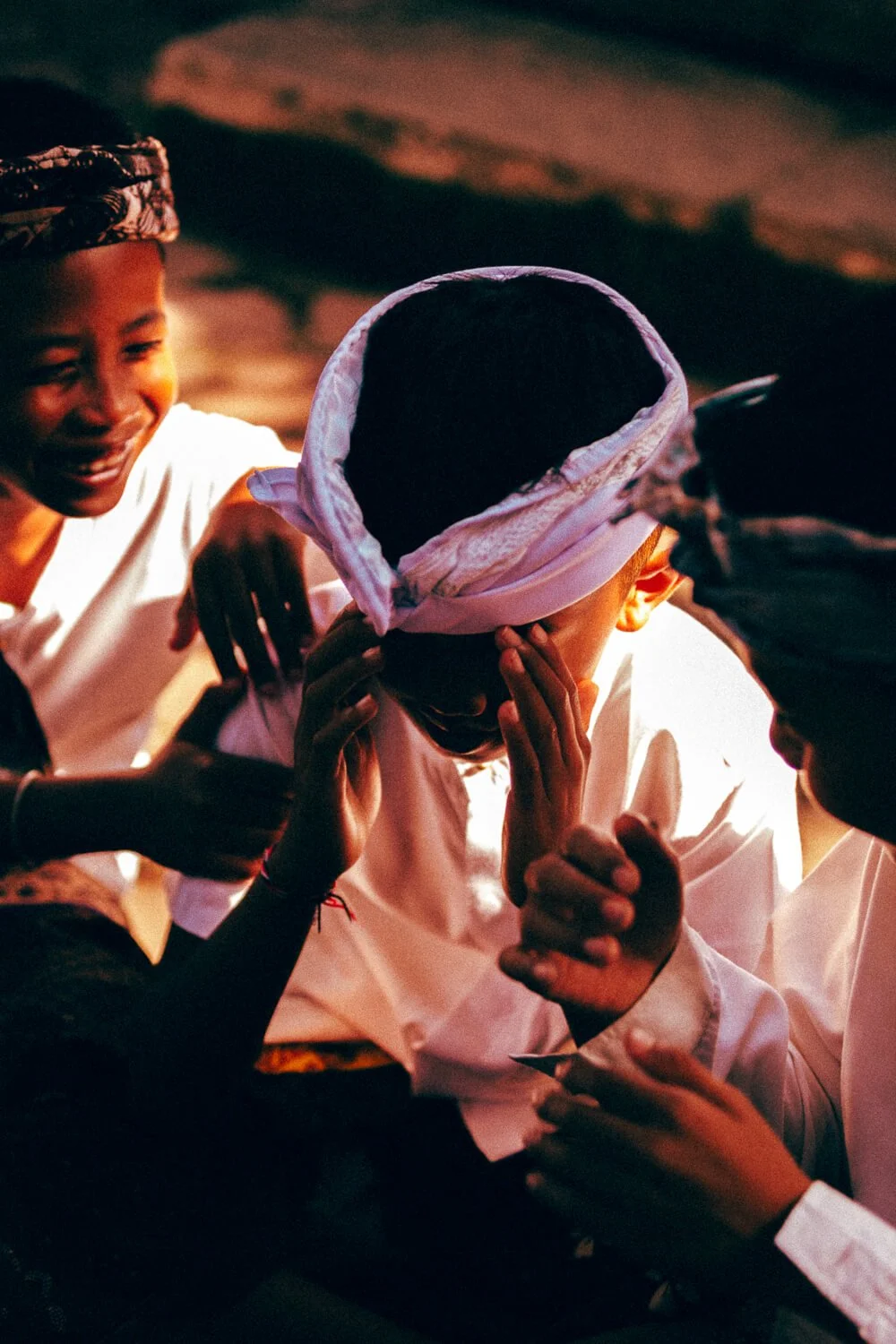 Groupe d'enfants souriants portant des vêtements traditionnels, échangeant des gestes amicaux lors d'une fête ou célébration à la tombée de la nuit.