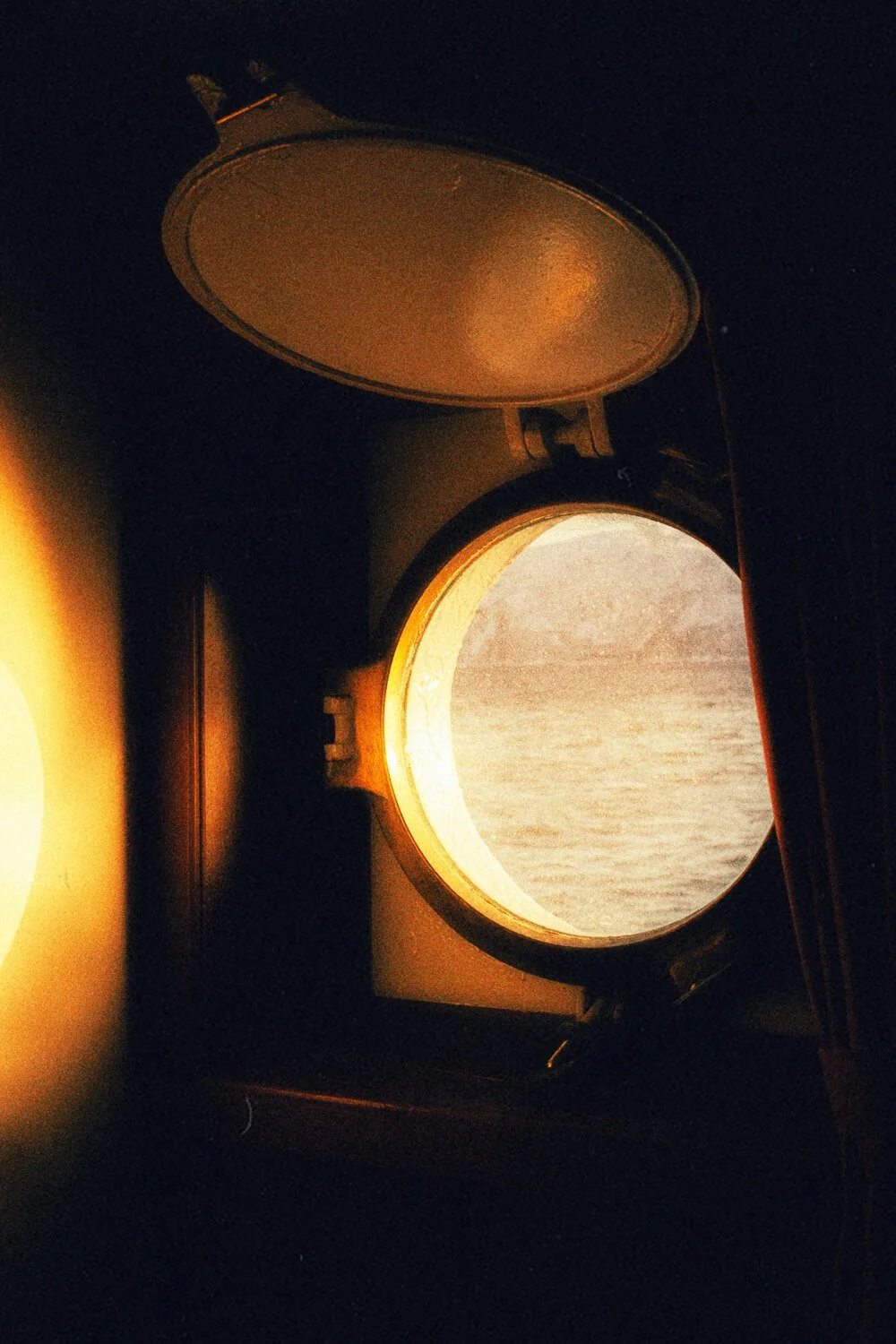 Vue depuis une fenêtre d'avion avec le hublot ouvert, montrant le ciel et la mer au coucher du soleil.