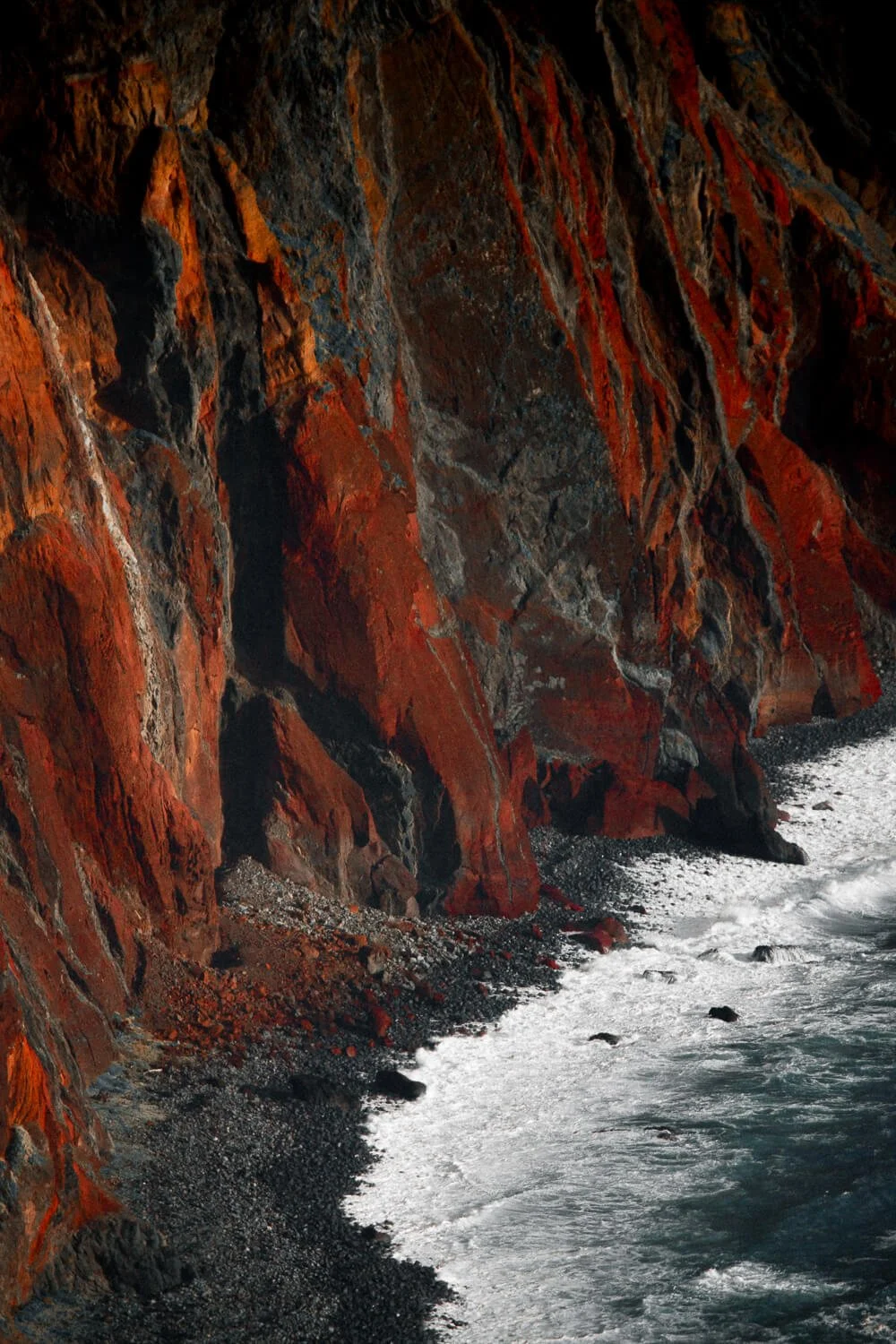 Falaises de roche rouge surplombant la mer avec des vagues qui s'écrasent contre la côte rocheuse.