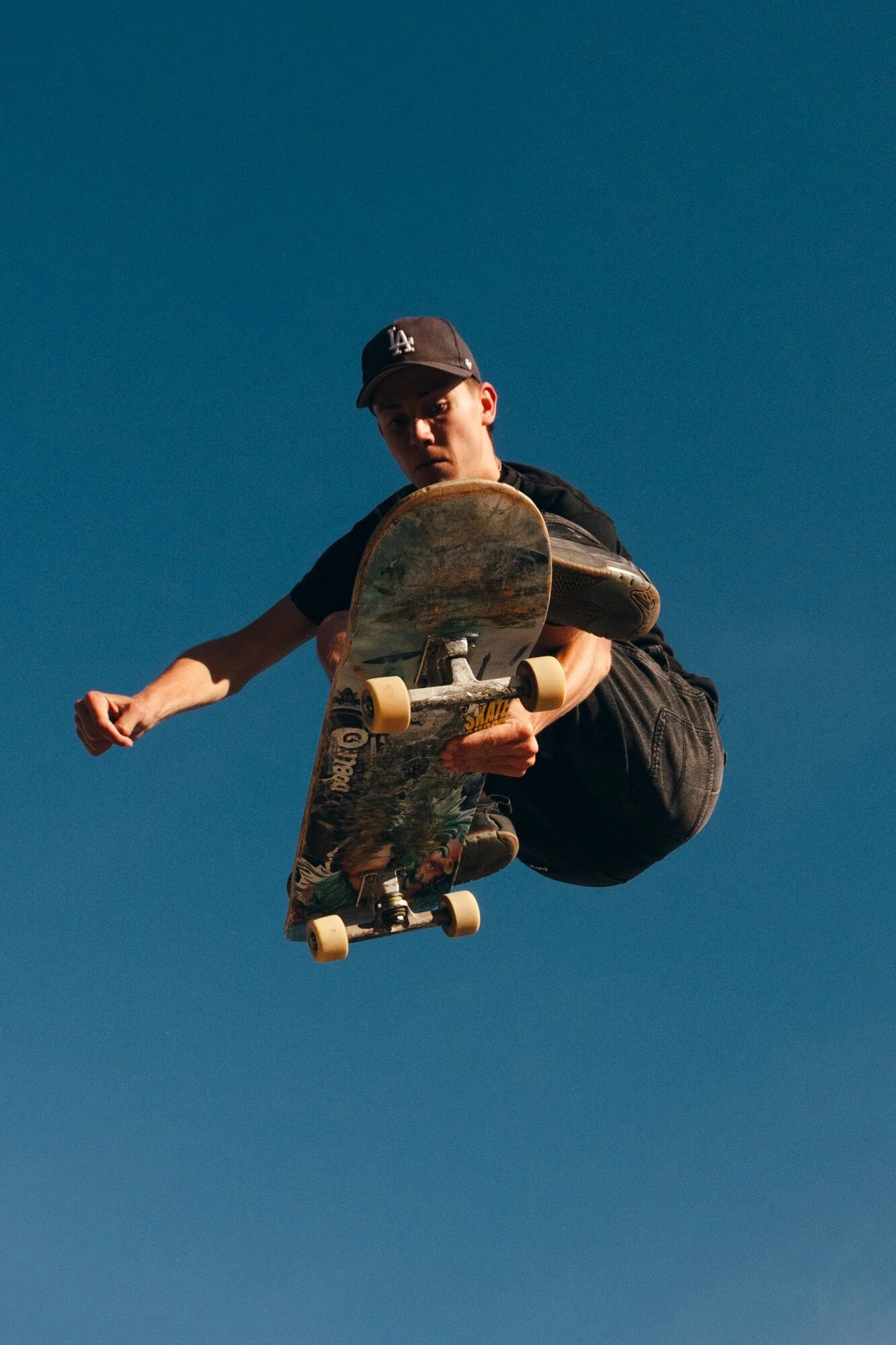 Skateboarder performing an aerial trick in midair against a clear blue sky.
