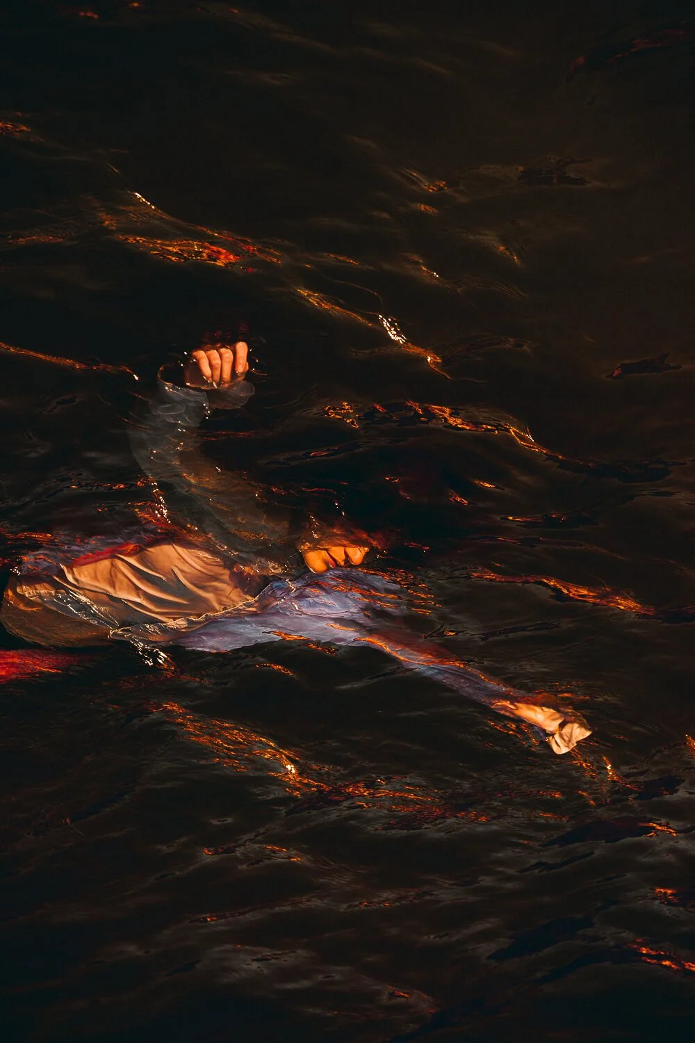 Person swimming in dark water at night with a hand emerging from the water.