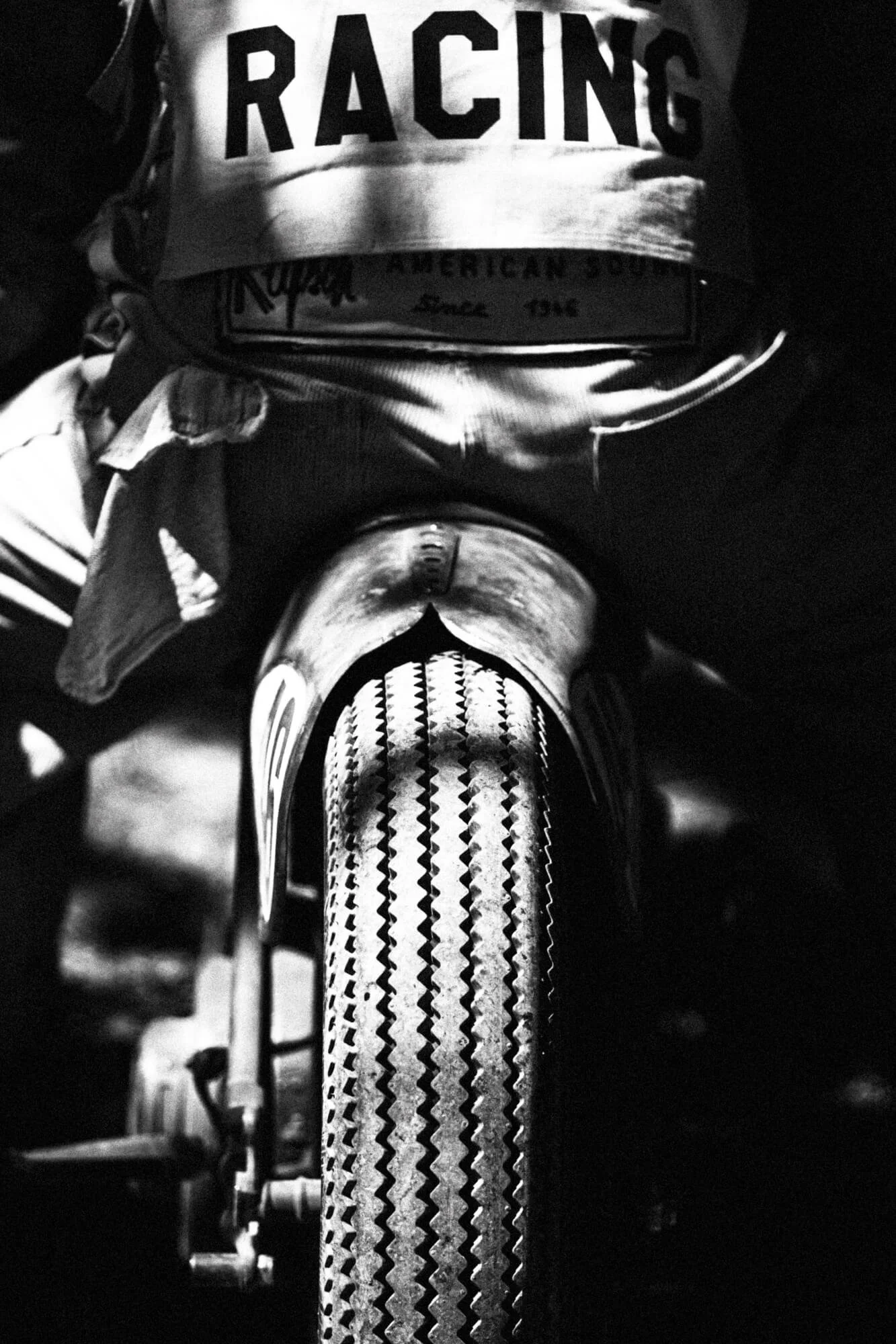 Close-up of a bicycle front tire with a rider wearing a racing jersey, focusing on the tire tread and part of the bike frame.