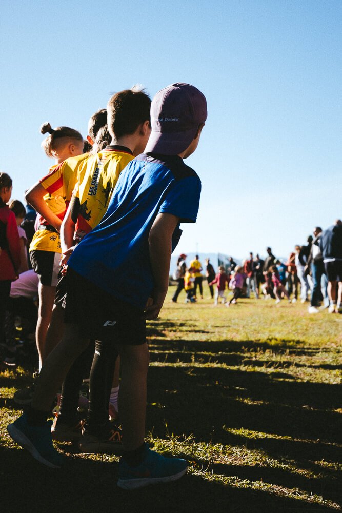 Children lined up outdoors on a grassy field, ready for a race during a sunny day.