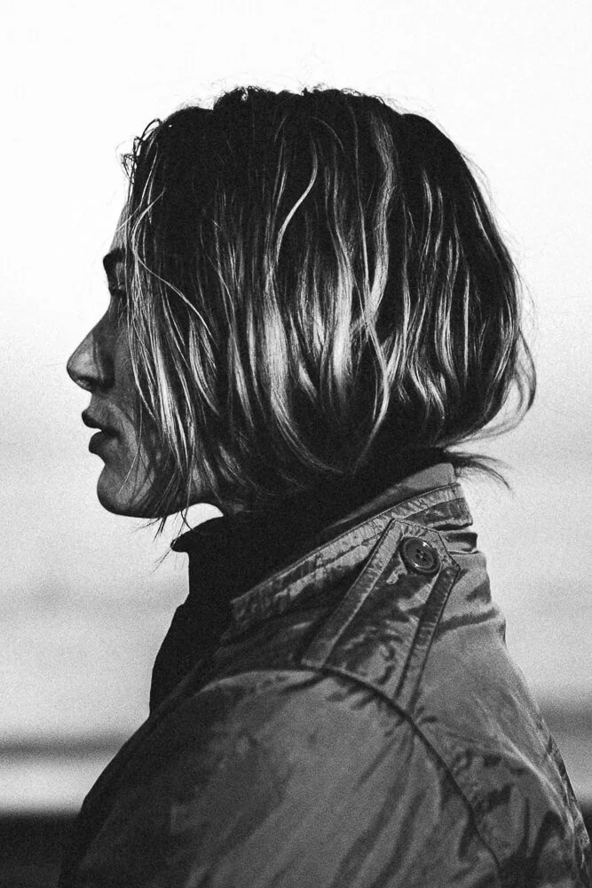 A woman with shoulder-length wavy hair looking to the left, wearing a jacket, in black and white.