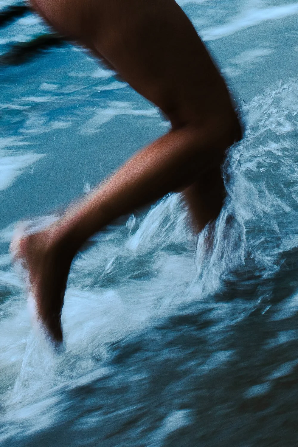 Close-up of a person's leg and foot while running in water, causing splashes.