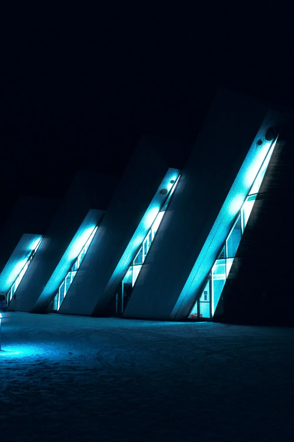 Bâtiment moderne avec façade en verre illuminée en bleu la nuit.