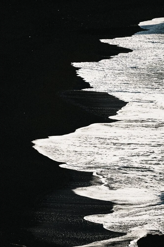 Black sand beach with white ocean waves crashing onto the shore.