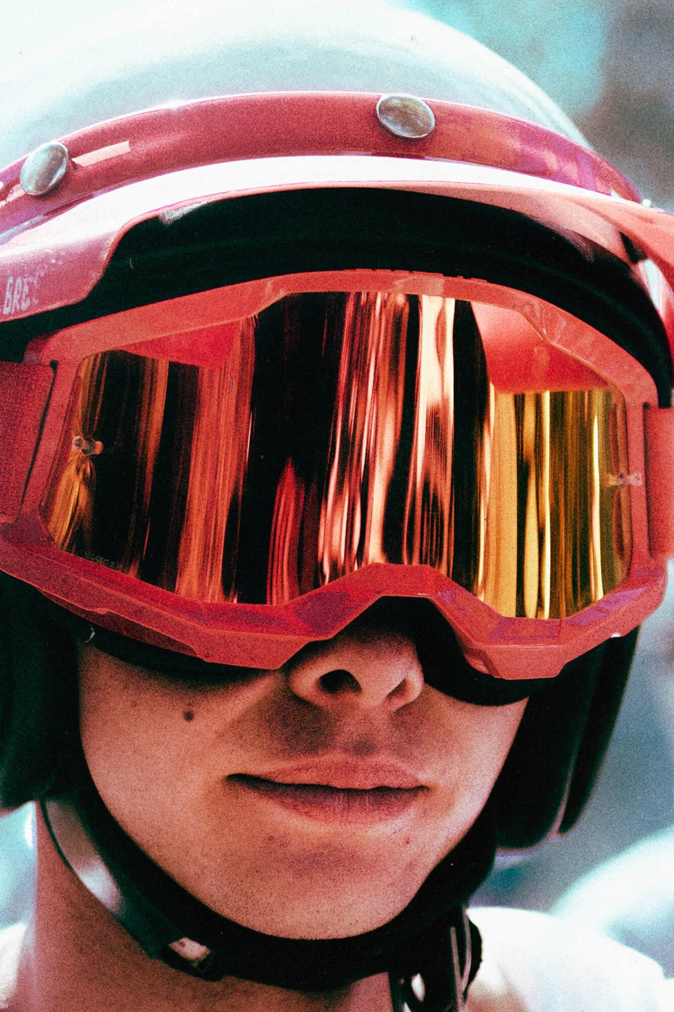 A person wearing red motorcycle goggles with reflective orange lenses and a black, padded strap.