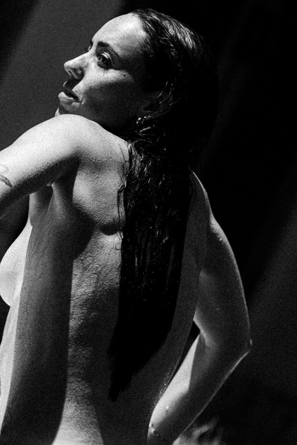 Black and white photograph of a woman with wet hair, her back partially turned, with water droplets on her skin.