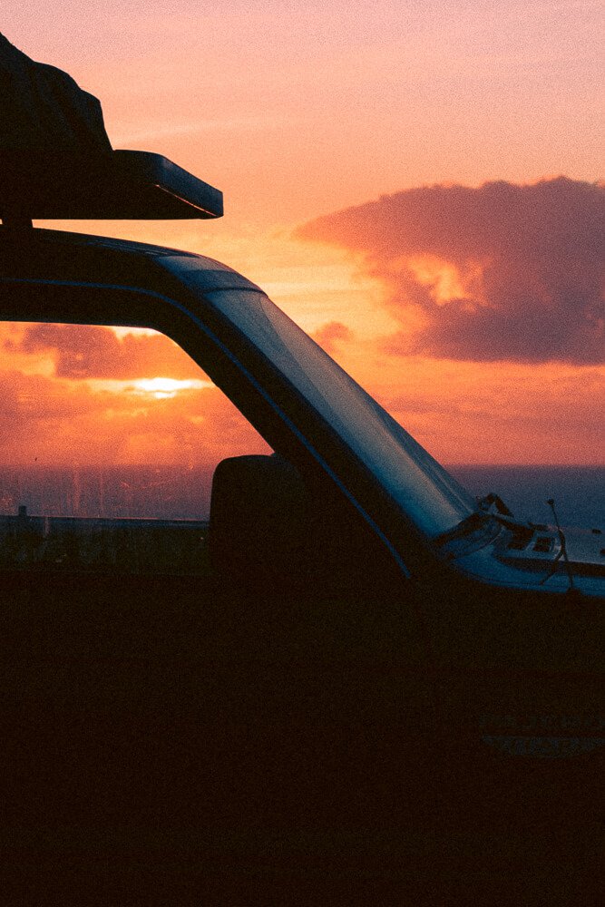 Part of a vehicle, possibly a helicopter, silhouetted against a vibrant sunset with orange and pink clouds.