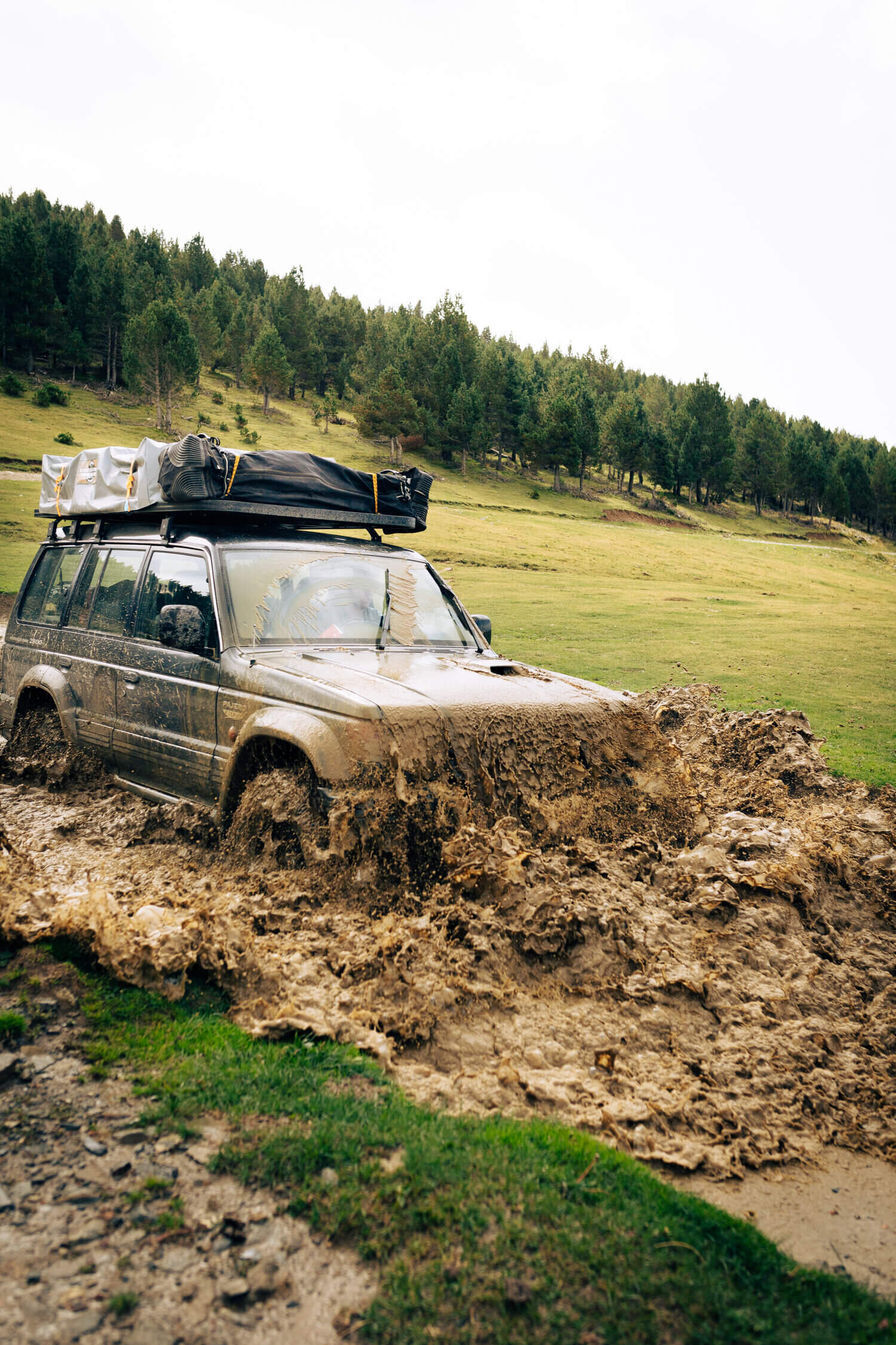 Voiture tout-terrain traversant une flaque de boue dans un paysage forestier.
