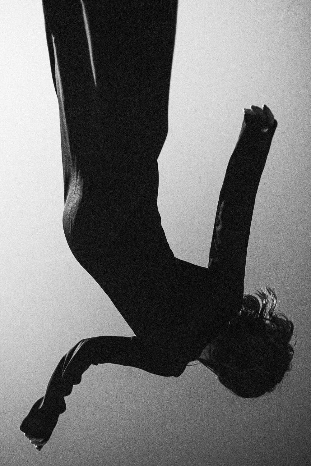 Black and white photo of a person with curly hair, sitting on a bench, leaning forward with hands clasped, viewed from the side.