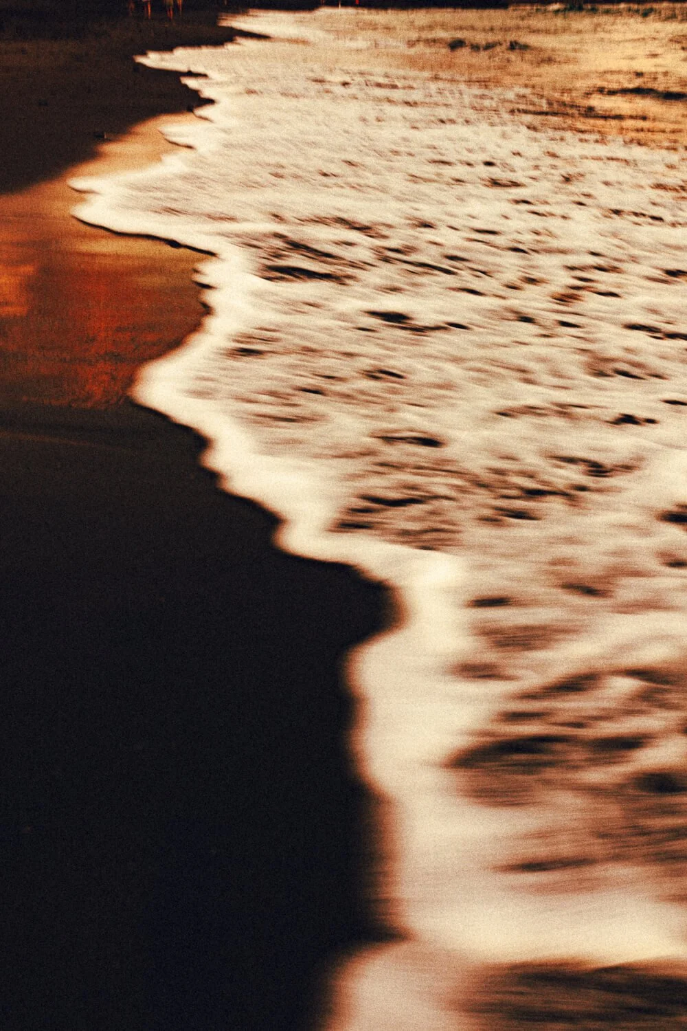 Vague image d'une plage au coucher du soleil avec du sable noir, des vagues et un horizon lumineux, ambiance calme et chaude.