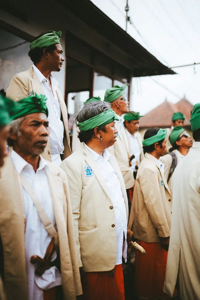 Group of people wearing beige jackets and green headwraps standing in a line outdoors.