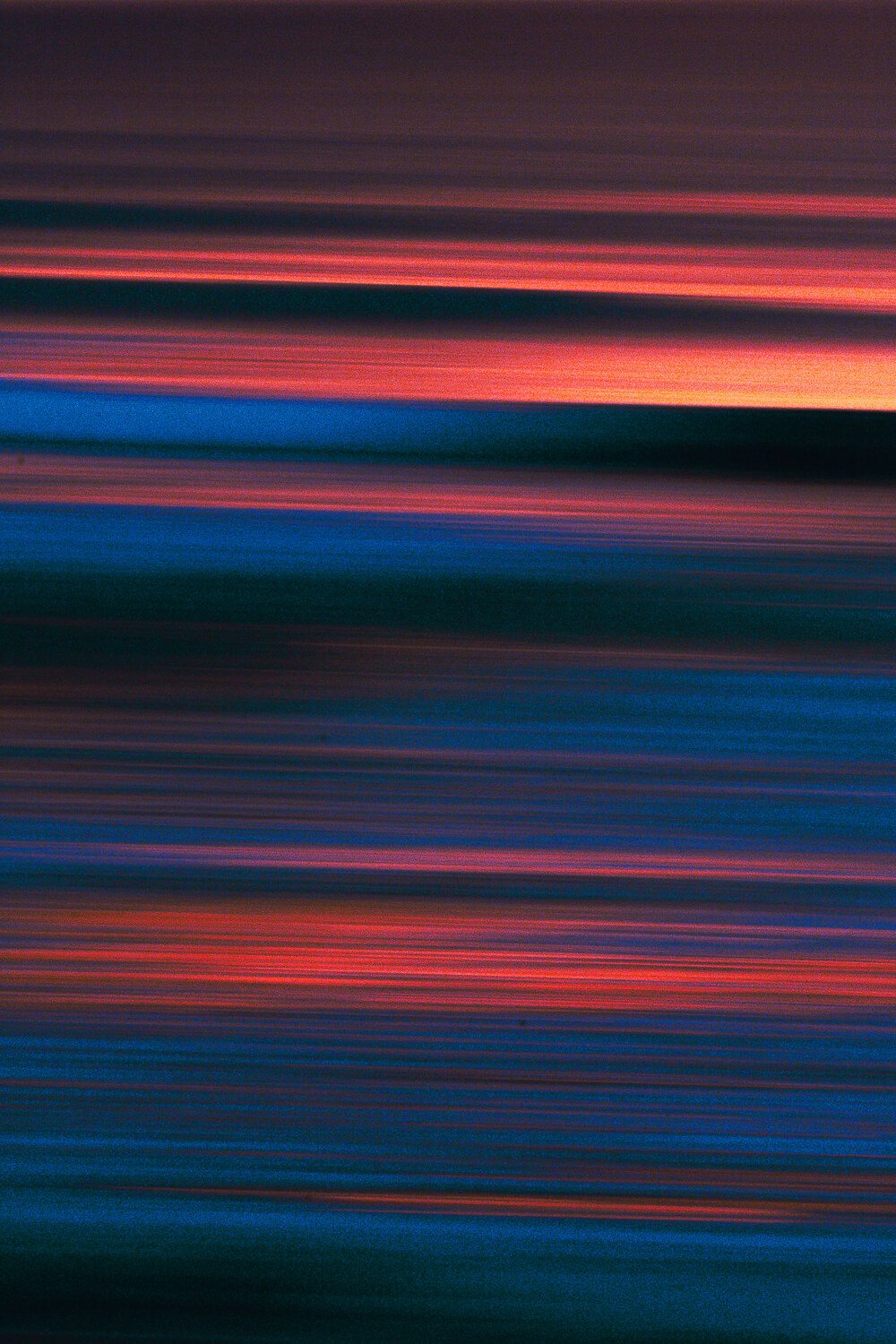 Blurred, horizontal streaks of red, pink, blue, and purple colors creating an abstract pattern.