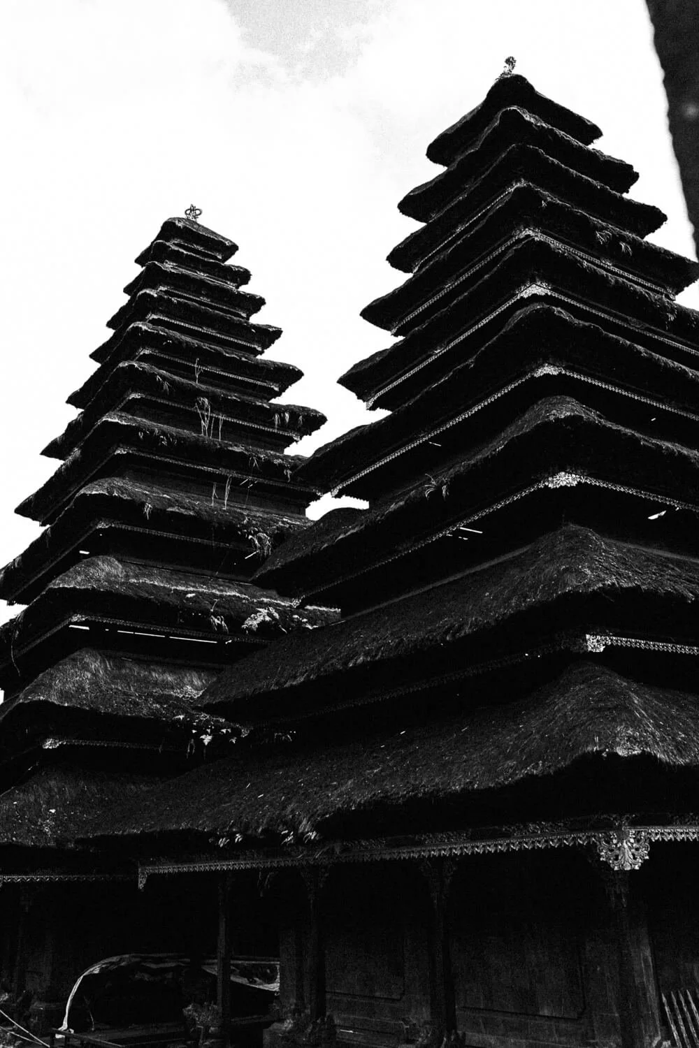 Deux toits de chaume en angle, avec de petites statues ou ornements en haut, sous un ciel gris.