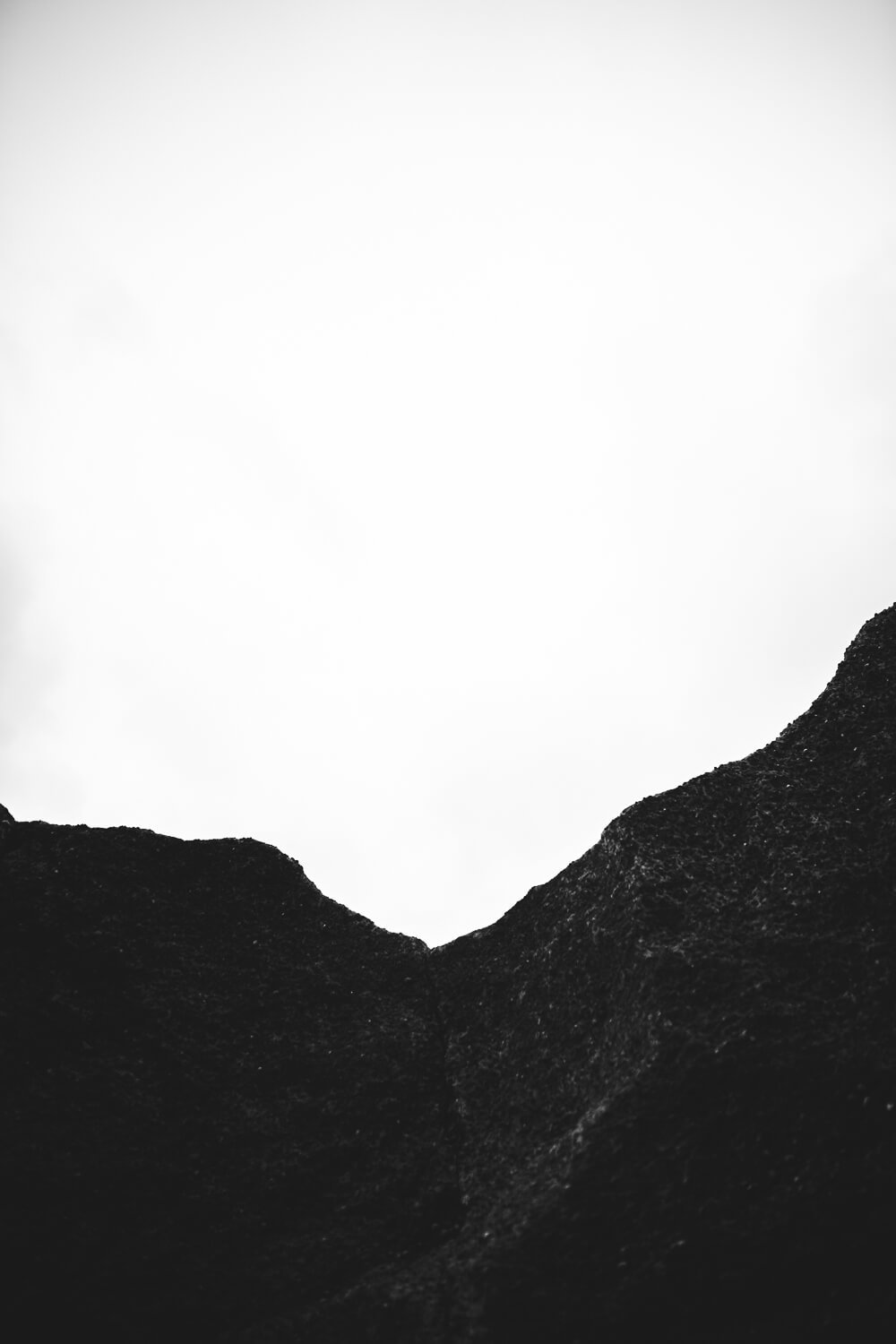 Black and white photograph of mountain peaks with a bright, possibly overcast sky in the background.