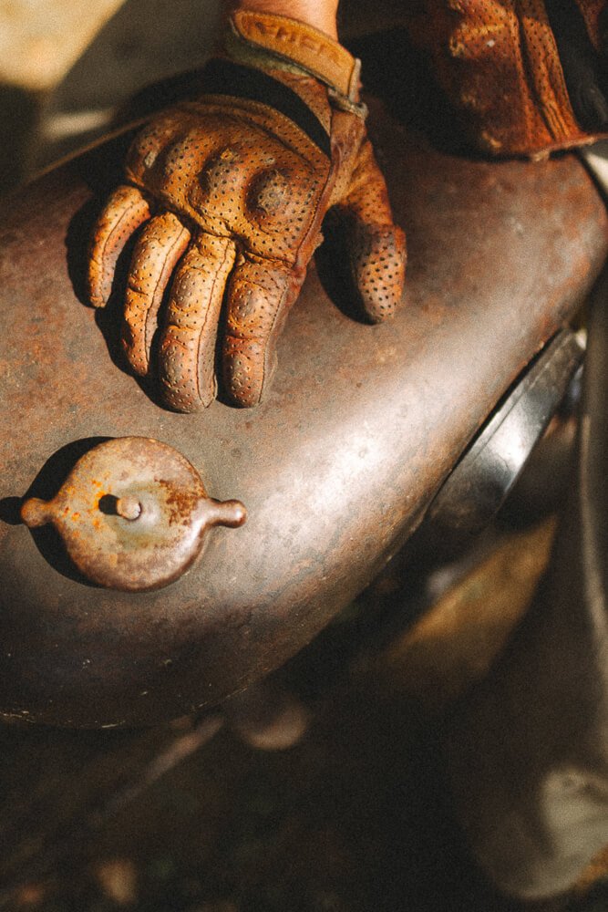 Close-up of a gloved hand resting on a rusty, metallic surface with a rusted, round object nearby.