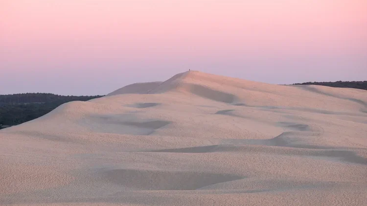 Dune de sable sous un ciel pastel rose et violet au crépuscule.