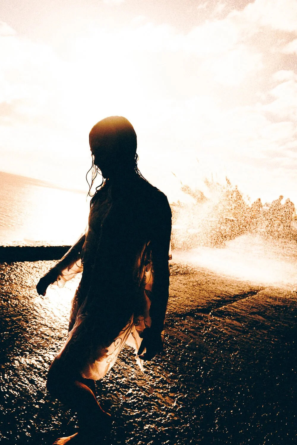 Silhouette of a woman walking in water with sunlight in the background.