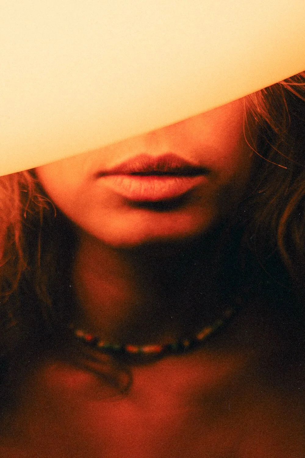 Close-up of a person's lips and chin, with part of their face partially obscured by a white opaque object, in warm lighting.